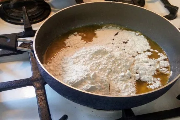 اضافه کردن روغن داغ به آرد در طرز تهیه حلوا با شیره انگور