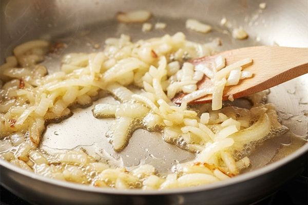 تفت دادن پیاز خردشده در روغن برای پاستا اسفناج با سس گوجه