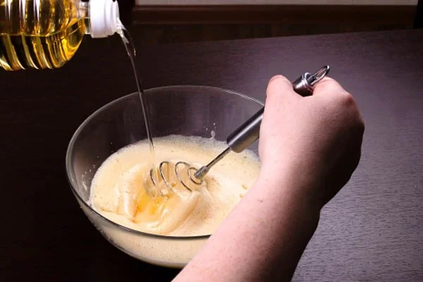 افزودن روغن به مخلوط تخم‌مرغ در تهیه کیک کاکائوی اسفنجی