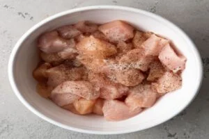 مزه‌دار کردن تکه‌های مرغ با نمک و فلفل در تهیه خورش کدو حلوایی