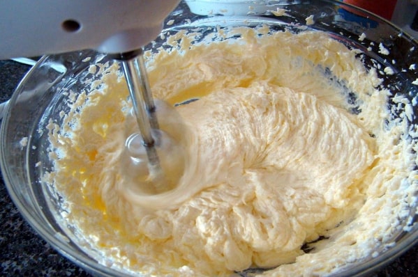 اضافه کردن خامه به مخلوط شکر و کره در تهیه فراستینگ کیک ساده