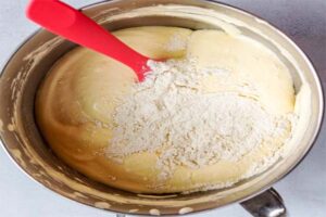 ریختن مخلوط آرد و سفیده تخم مرغ در ظرف مخلوط زرده در تهیه کیک عید قربان