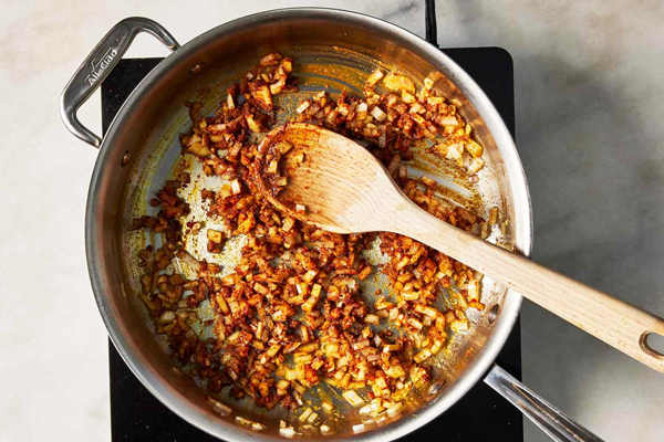 اضافه کردن ادویه و رب گوجهفرنگی به پیاز و سیر تفت داده شده