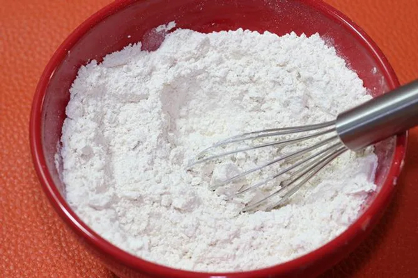 مخلوط کردن آرد و بیکینگ‌پودر در تهیه پنکیک موزی بدون تخم مرغ