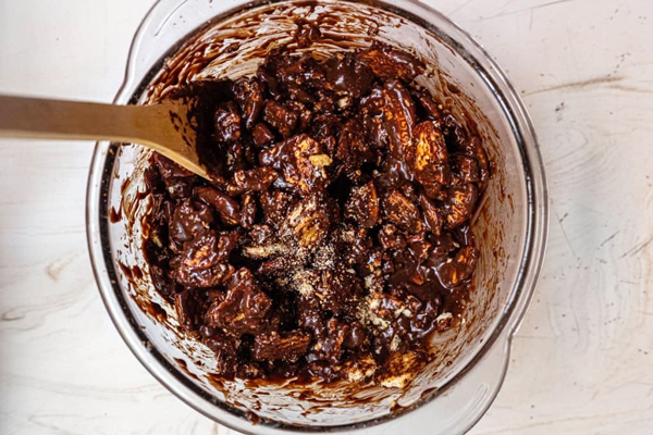 اضافه کردن بیسکویت خرد شده به مخلوط کاکائو در تهیه کیک یخچالی با بیسکویت خرد شده