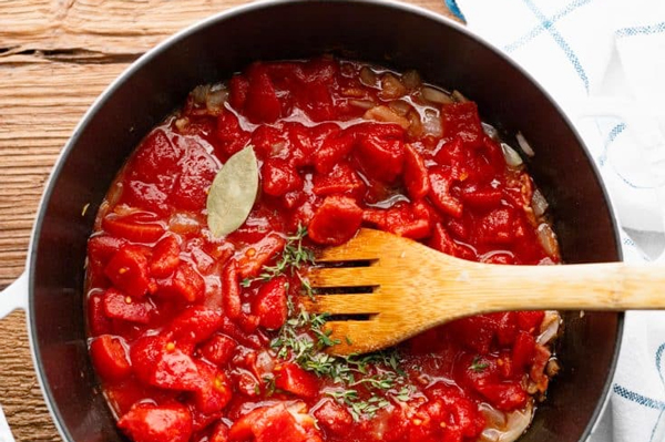 اضافه کردن گوجه فرنگی خرد شده، سس و طعم‌دهنده به خورشت بامیه با گوجه