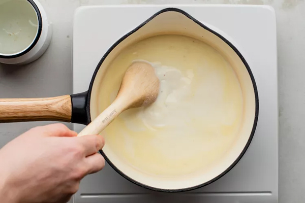 اضافه کردن شیر به مخلوط در تهیه سس پنیر چدار