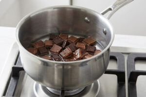 ریختن تکههای شکلات تلخ و شیرین در قابلمه برای تهیه موس شکلات و خرمالو