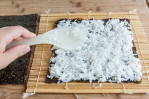 ریختن برنج سوشی روی جلبک دریایی در تهیه سوشی