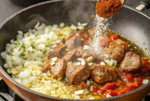 تفت دادن گوشت تکه‌ای با ادویه‌ها و رب گوجه فرنگی برای خورشت بامیه با تمبرهندی