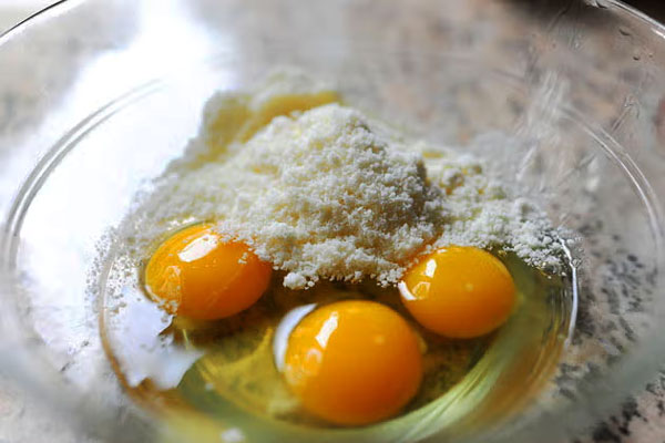 ترکیب تخم مرغ و پنیر پارمزان در کاسه برای تهیه اسپاگتی کاربونارا