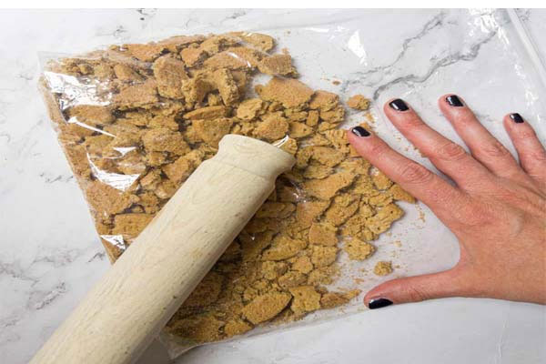 خرد کردن بیسکوییت وانیلی با گوشت کوب برای تهیه شیرینی 