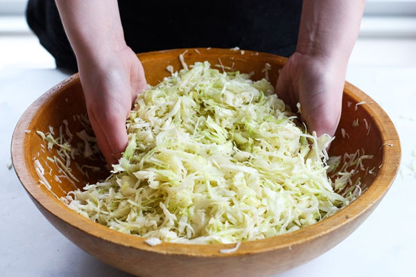 ماساژ دادن کلم با دست در کاسه چوبی