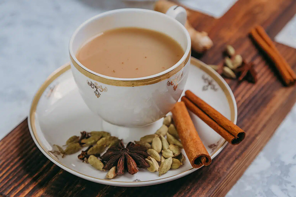 یک فنجان چای ماسالا با شیر درکنار دارچین و هل