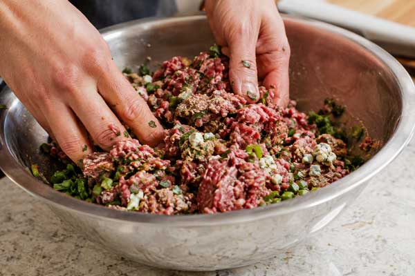مخلوط کردن گوشت چرخکرده با مواد اولیه برای تهیه مایه برگر با پنیر بلوچیز
