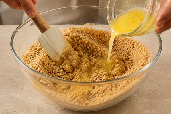 مخلوط کردن بیسکویت خردشده با کره ذوب‌شده در تهیه چیز کیک کاراملی کاتلا