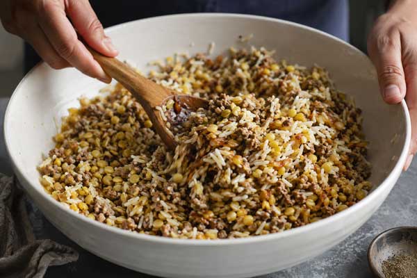 مخلوط کردن گوشت تفت داده‌شده، برنج، لپه و پیاز برای تهیه مواد میانی گیپای کرمانی