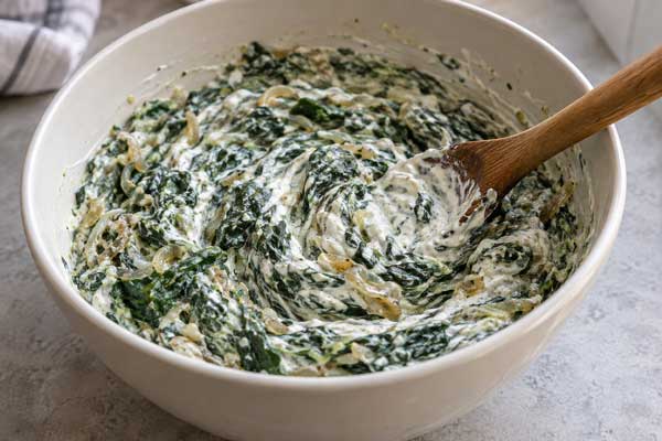 افزودن ماست چکیده، فلفل سیاه، سیر و نمک به مخلوط بورانی اسفناج با پیاز داغ