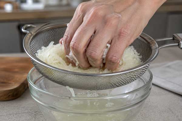رنده کردن پیاز و گرفتن آب اضافه آن برای تهیه کوکو سیب زمینی با پنیر پارمسان
