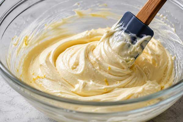 مخلوط کردن پنیر خانهای، شکر، نشاسته ذرت و زرده تخم مرغ برای تهیه کرم پنیری گلت تابستانی